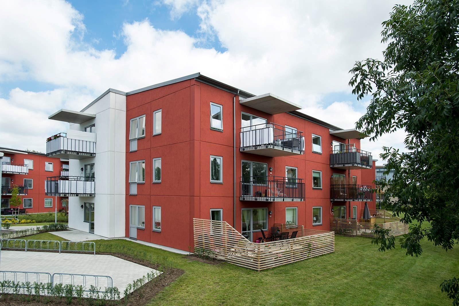 En modern bostadsbyggnad med tre våningar, målad i en röd färg med vita accenter runt fönstren och 