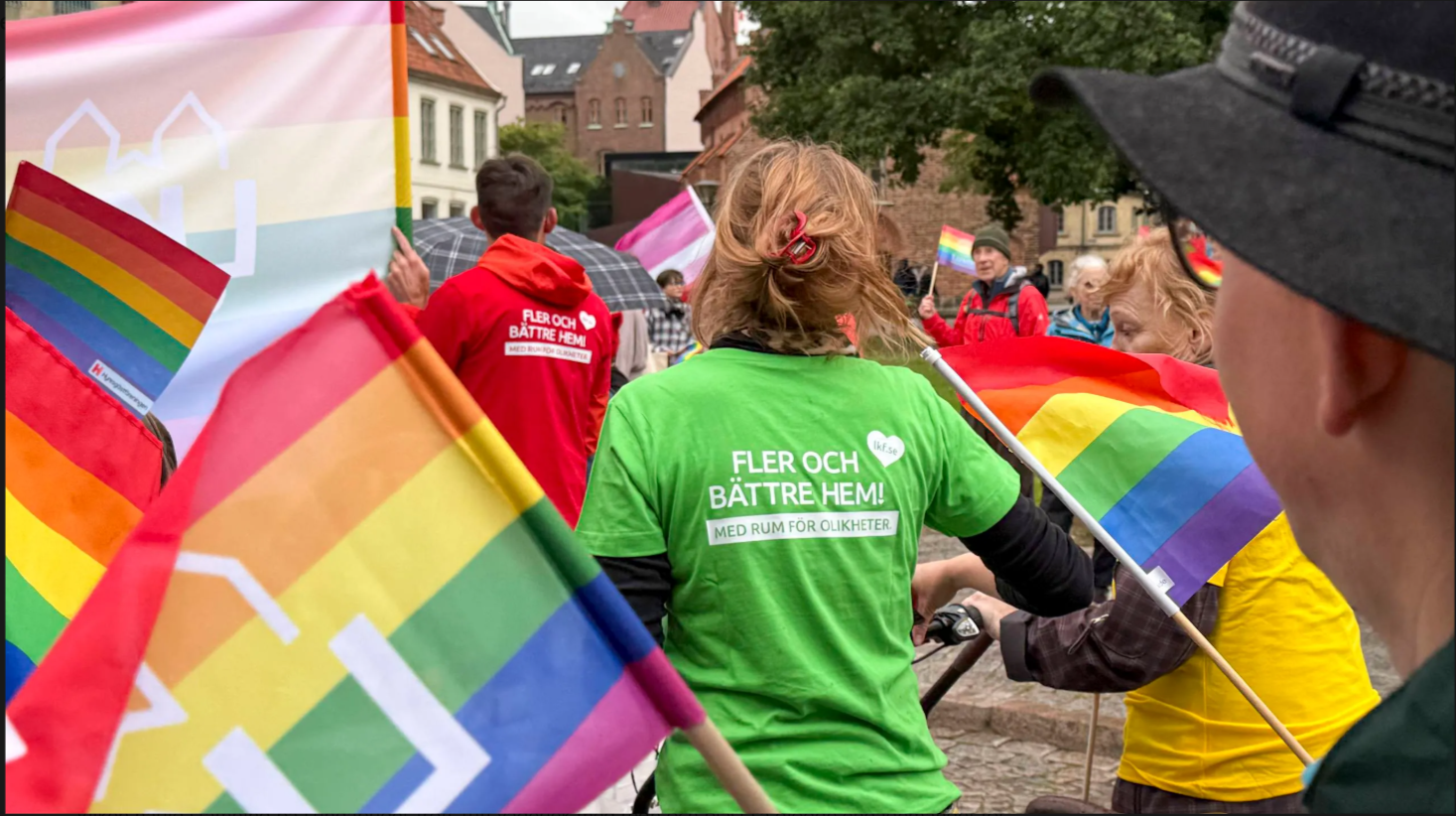 person i hatt i förgrunden, flaggor och grön t-shirt med budskap i bakgrunden under lundapride 2026