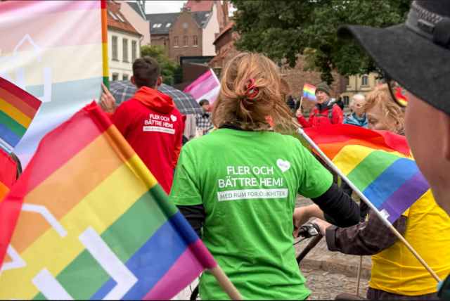 person i hatt i förgrunden, flaggor och grön t-shirt med budskap i bakgrunden under lundapride 2026
