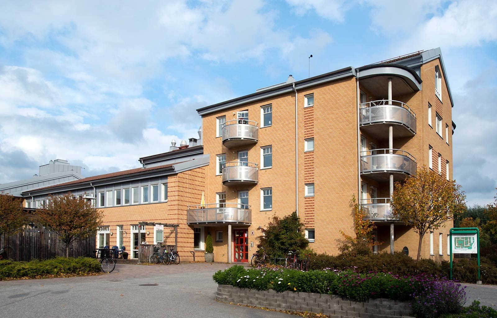 En gul tegelbyggnad med tre våningar och rundade balkonger på höger sida. Det finns cyklar parkerad