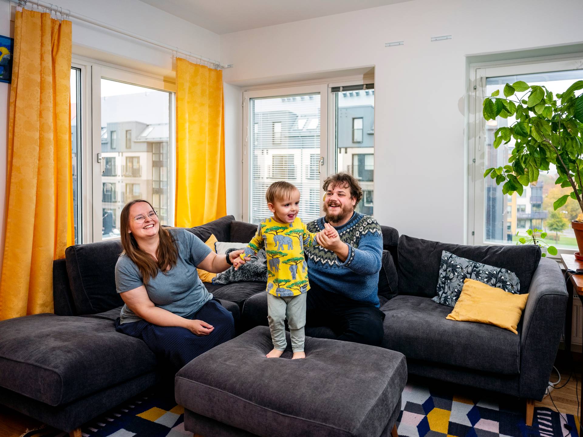 Bilden visar en mamma och pappa i en hörnsoffa med sitt lilla barn. 