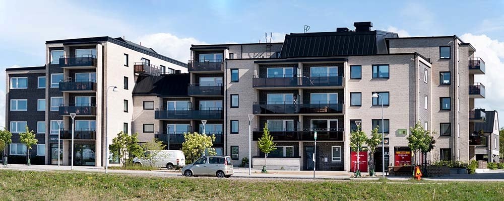 Ett modernt flerbostadshus med ljusa och mörka ytor, balkonger med glasräcken och stora fönster. Tv