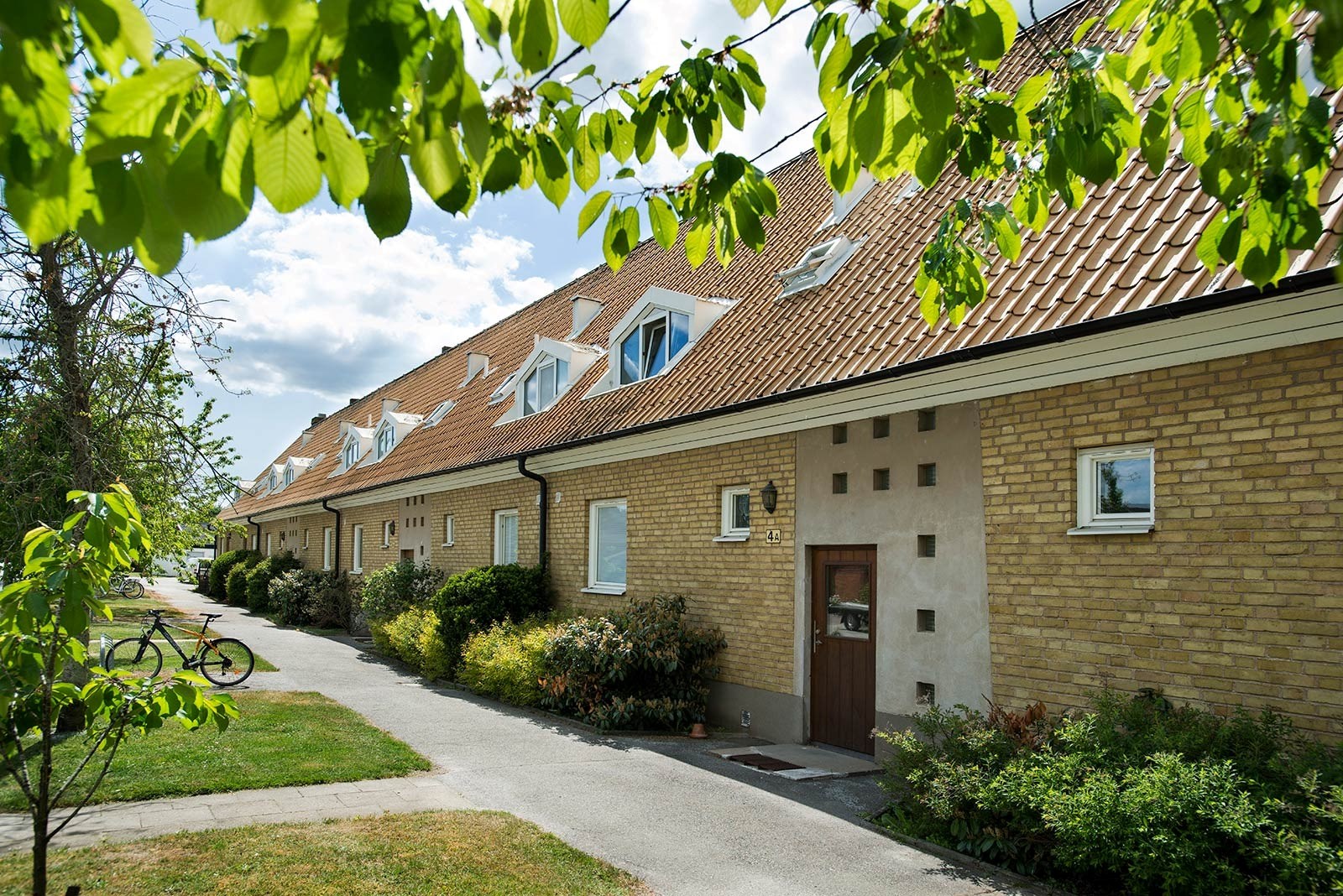 En rad sammanlänkade hus med gula tegelväggar och bruna tak. Varje hus har små fönster och en trädö