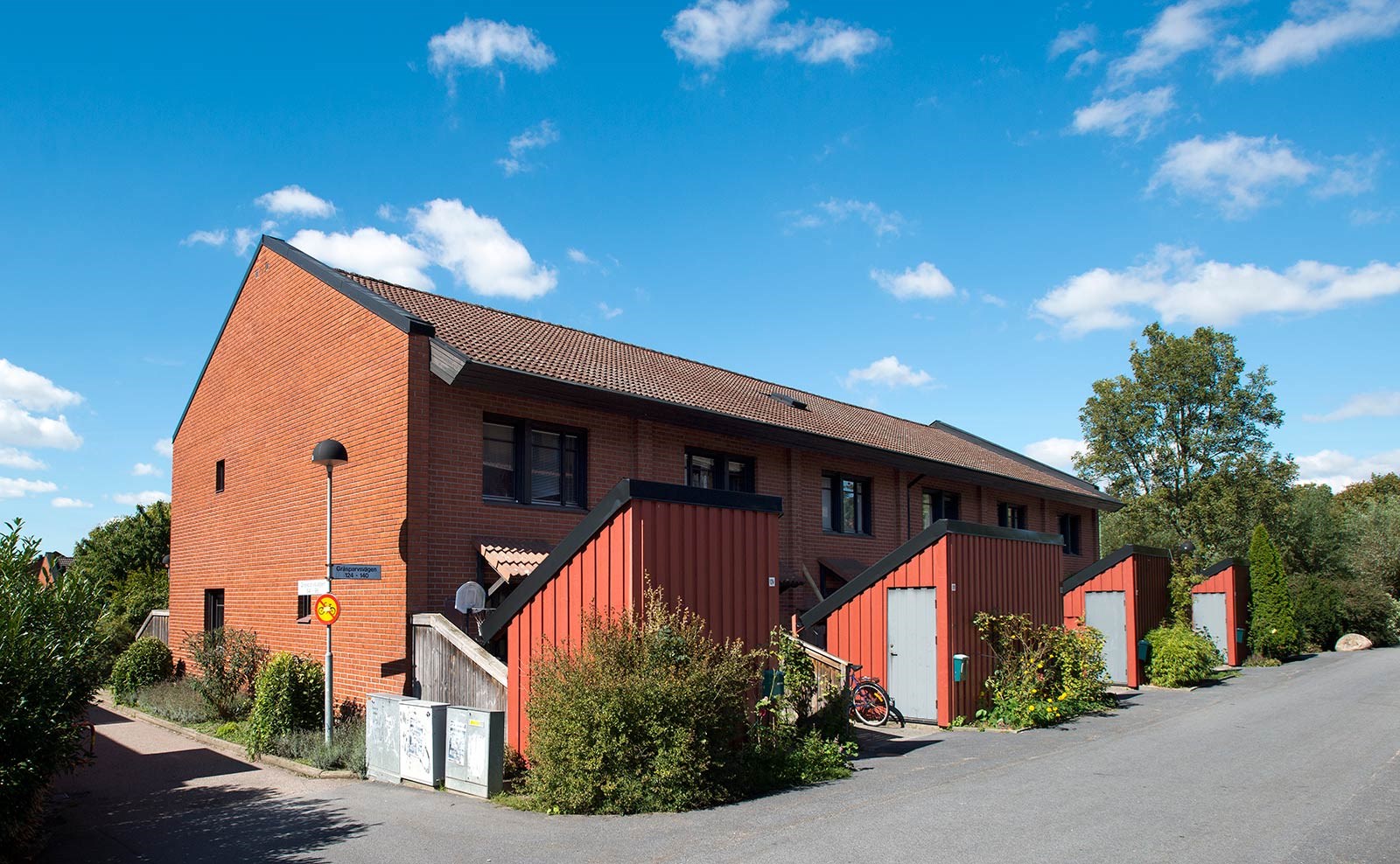 Radhus i två plan med enskilda röda förrådsbyggnader vid varje entré.