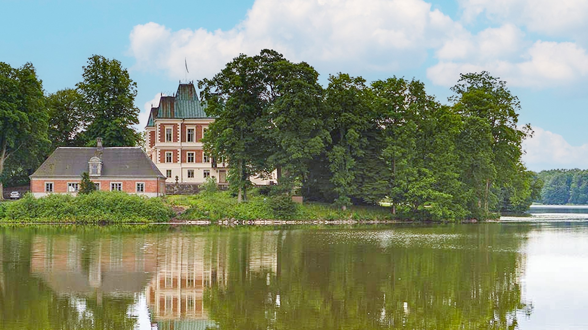 Bild på ett gammalt gods på en udde. Reflekteras i sjön.