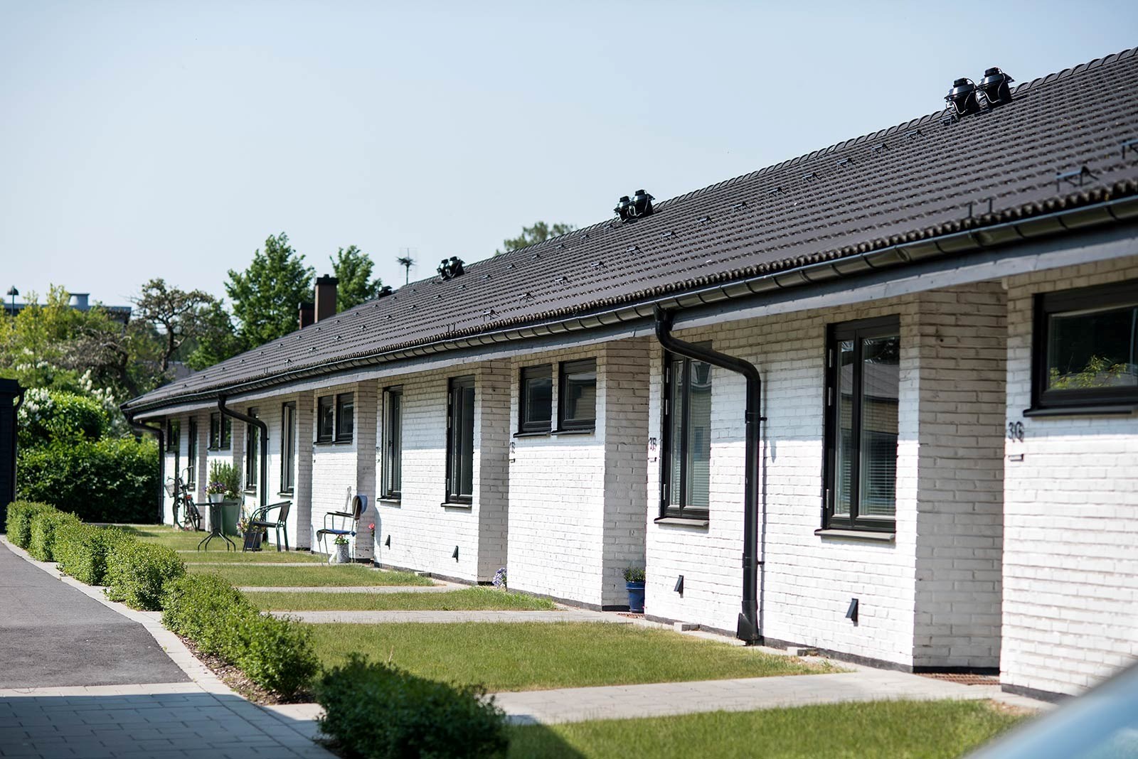 Framsidan av en radhuslänga i ett plan. Fasaden är av vitt tegel och framför varje ingång finns en liten gräsplätt.