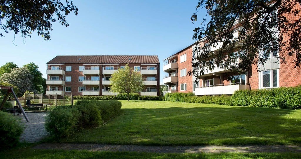 Två huskroppar med flerfamiljshus i tre våningsplan. Mellan husen är det en stor grönyta samt en lekplats.