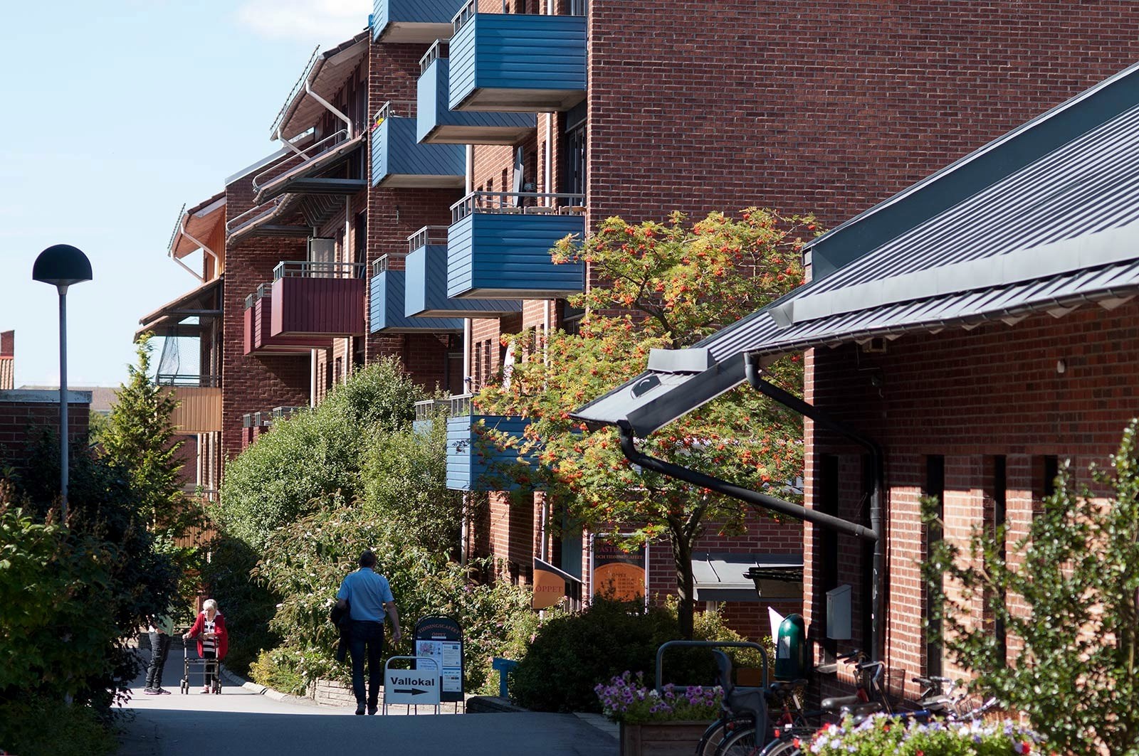 Ett bostadsområde med flerfamiljshus med färgglada balkonger. Framför huset finns en gångväg omringad med grönska.